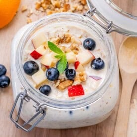 a mason jar with overnight oats topped with chopped apples, blueberries, and walnuts.