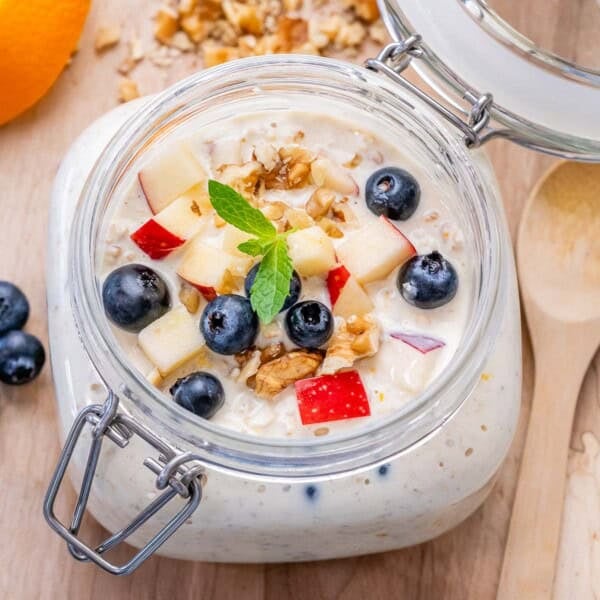 a mason jar with overnight oats topped with chopped apples, blueberries, and walnuts.