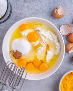 Mixing bowl filled with cream cheese, sugar, eggs, cinnamon, and vanilla ready to be blended for pumpkin cheesecake filling.