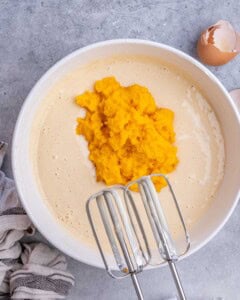 Creamy cheesecake mixture in a bowl with pumpkin puree added on top, ready to be mixed together.
