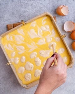 Baking dish lined with crust, as pumpkin and plain cheesecake batters are being swirled together before baking.