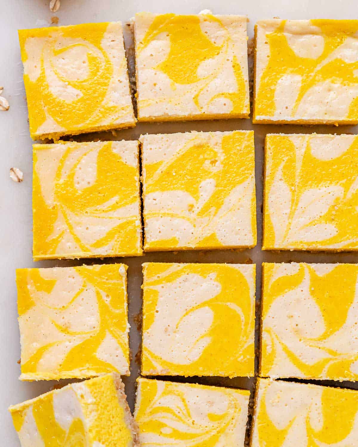 Pumpkin cheesecake bars sliced evenly into neat squares on parchment paper after cooling.