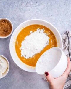 hand pouring flour over the wet pumpkin batter.