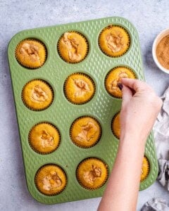 Sprinkling cinnamon sugar over pumpkin muffins in a pan.
