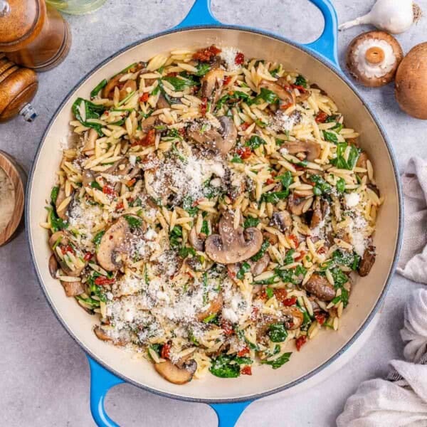 Overhead view of Mushroom Spinach Orzo sprinkled with parmesan cheese in a skillet.