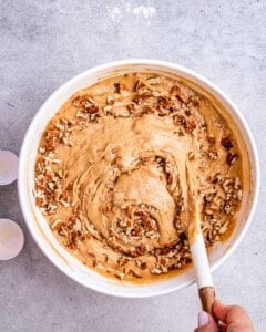 Batter being mixed in a large bowl with chopped pecans folded in for texture.