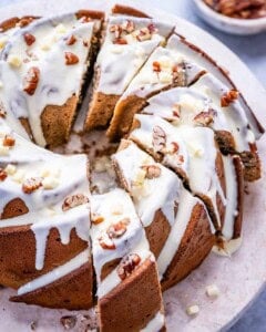 Overhead shot of a sliced sweet potato Bundt cake topped with creamy white chocolate glaze and chopped pecans on a marble surface.