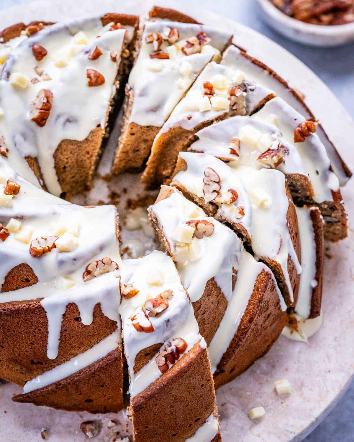 Overhead shot of a sliced sweet potato Bundt cake topped with creamy white chocolate glaze and chopped pecans on a marble surface.