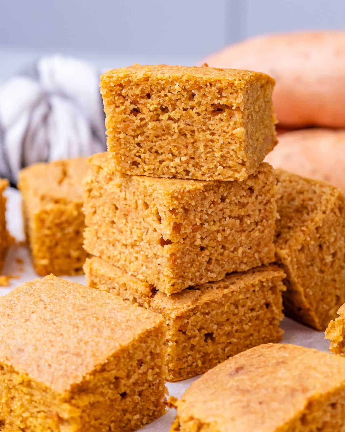 A close-up of sliced sweet potato cornbread squares stacked together, showing their soft, tender crumb.