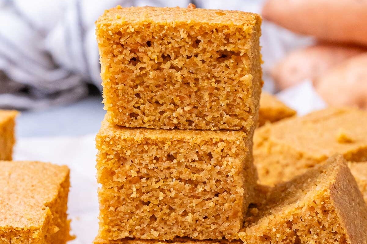 A stack of thick, golden sweet potato cornbread pieces balanced on a cutting board.