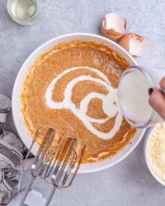 Buttermilk being poured into the sweet potato mixture while it’s whisked to create a smooth, creamy batter.