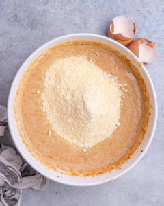 Cornmeal sitting on top of the wet sweet potato mixture before being stirred in, showing the start of combining the dry and wet ingredients for the cornbread batter.