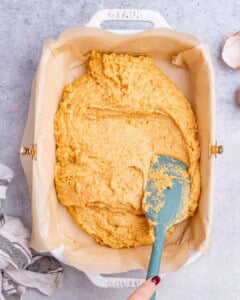 The cornbread batter being spread evenly into a parchment-lined baking dish with a spatula.