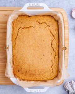 A full baking dish of golden-brown sweet potato cornbread just out of the oven, still warm and slightly cracked on top.