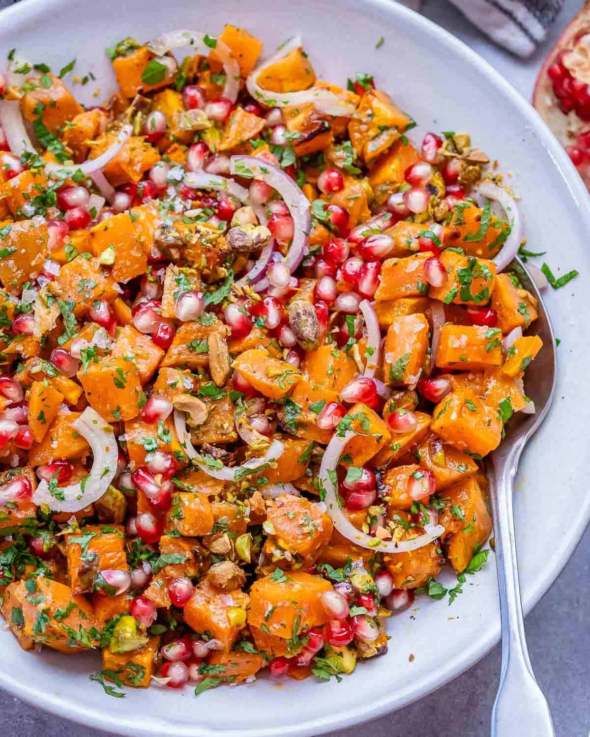 Overhead view of vibrant sweet potato salad with herbs, pistachios, red onion, and pomegranate seeds in a serving bowl.