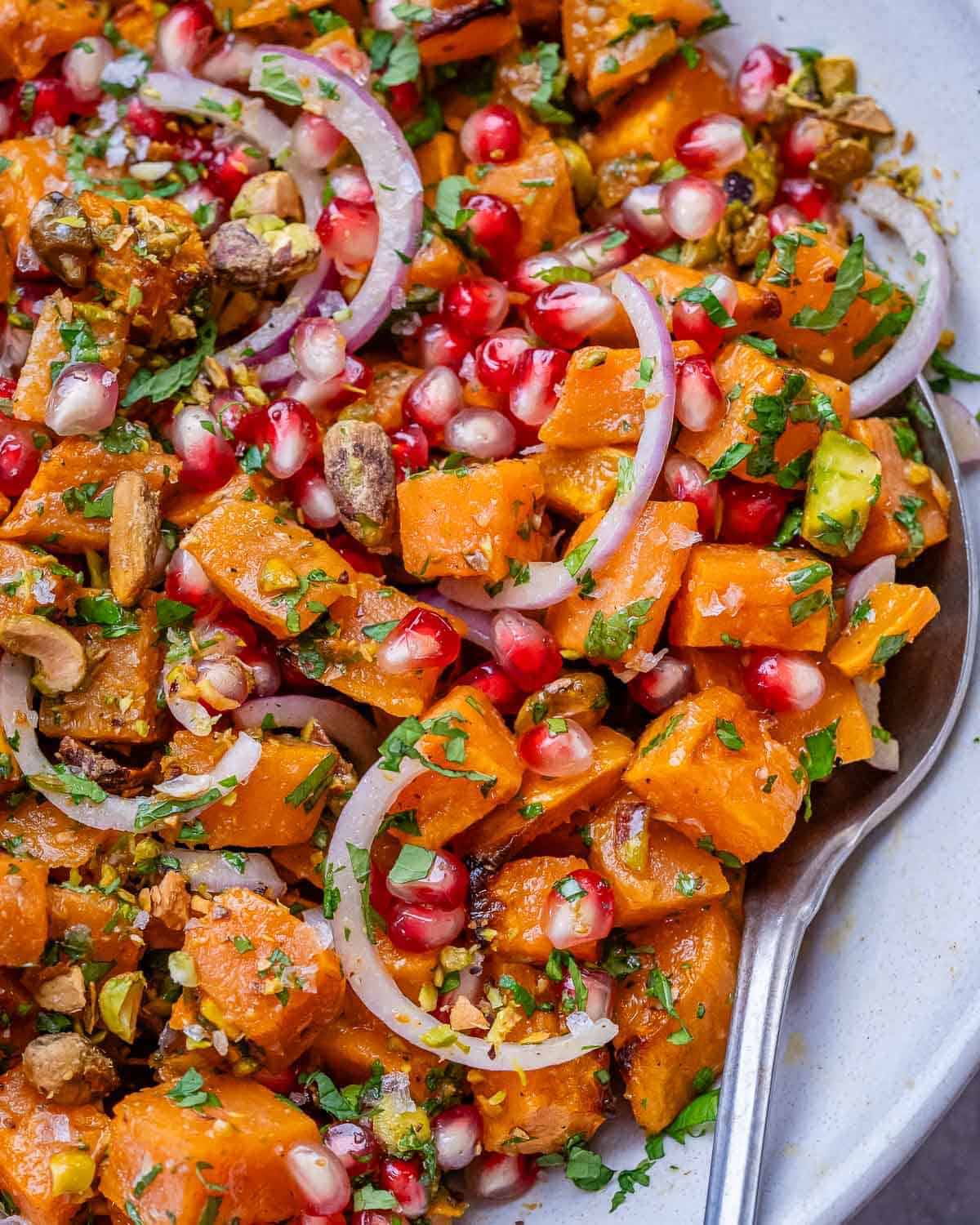 Close-up of sweet potato salad showing roasted cubes mixed with pomegranate seeds, red onion, parsley, and dressing.