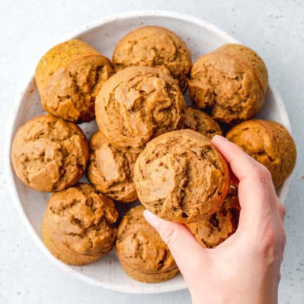 hand grabbing a single pumpkin banana muffin from a bowl filled with them.