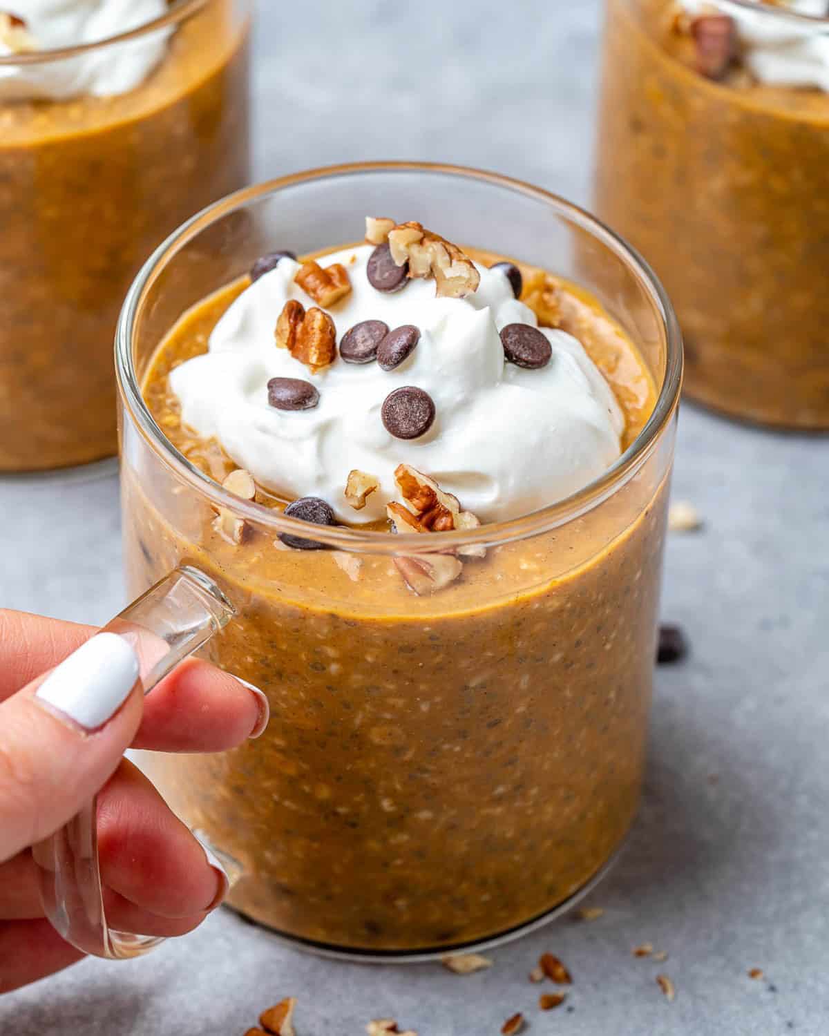 hand holding a cup filled with pumpkin overnight oats.