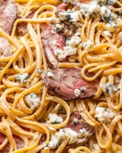 pasta and steak in a pan topped with crumbled blue cheese.