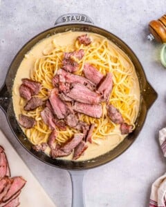 Steak added over creamy pasta in the skillet.