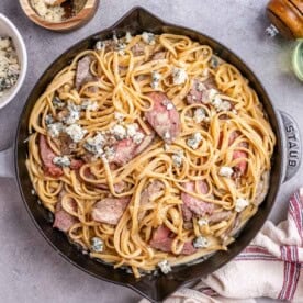 pasta with steak slices in a skillet topped with crumbled blue cheese.