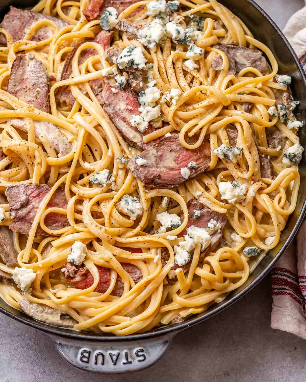 creamy pasta with steak bites in a skillet topped with crumbled blue cheese.
