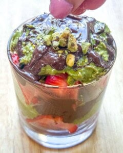 adding chopped pistachios on top of the Dubai strawberry cup.