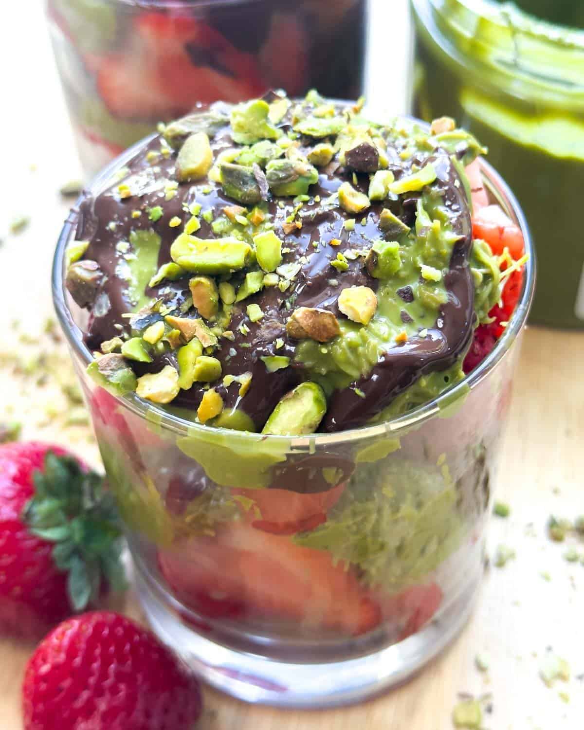 a cup with layers of chopped strawberry, pistachio kataifi, and melted chocolate.