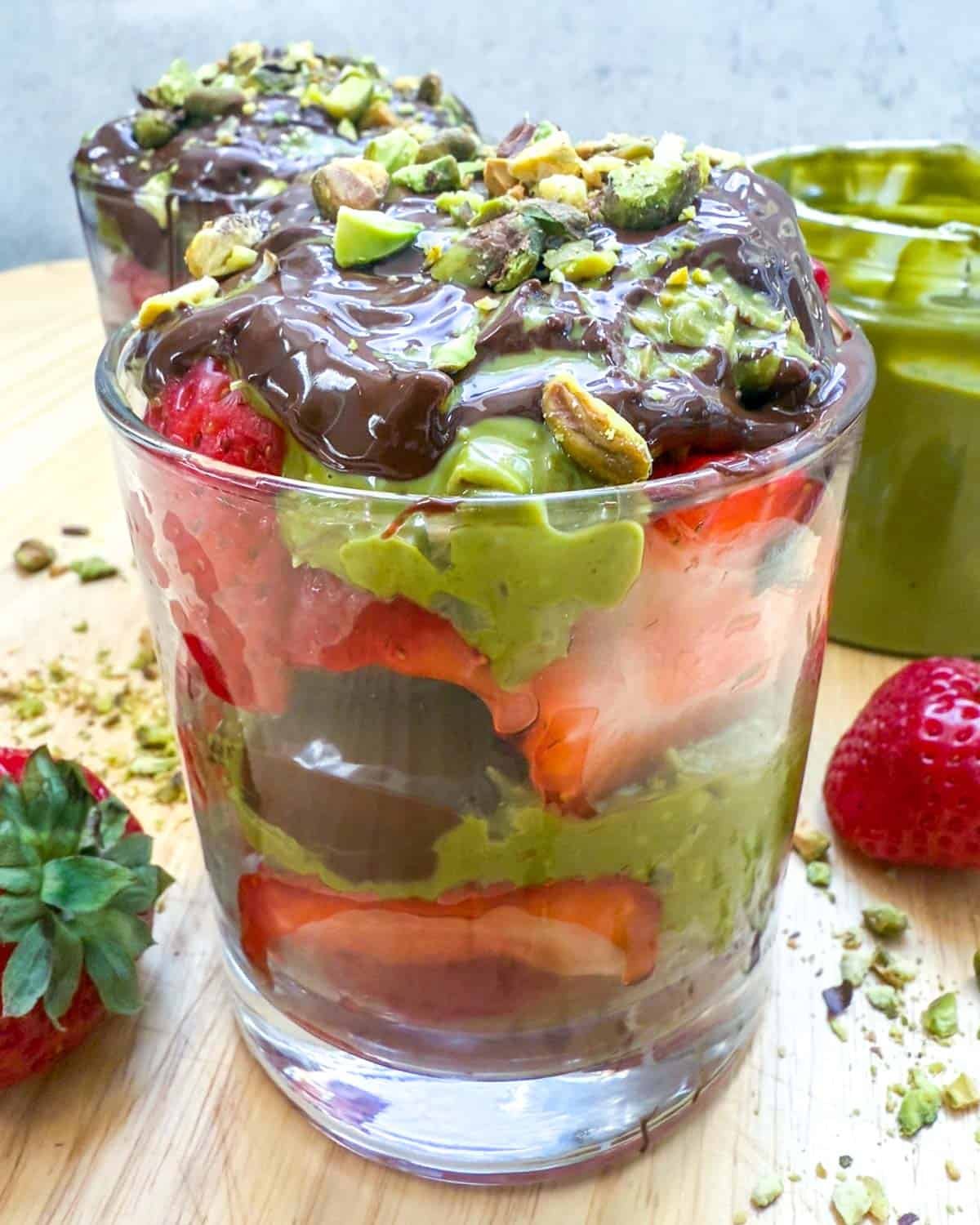 a cup layered with strawberries, crunchy pistachio cream, and melted chocolate.
