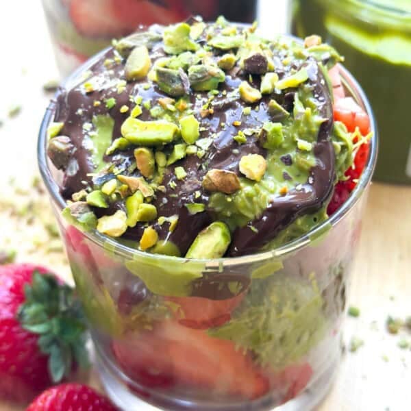 a cup filled with strawberries, pitachio cream crunch, melted chocolate, and topped with crushed pistachio.