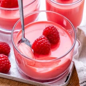 red looking yogurt jello in a cup topped with 2 raspberries.
