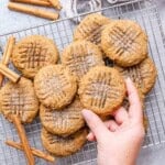 cookies on a cooling rack with one hand reaching for a cookie.