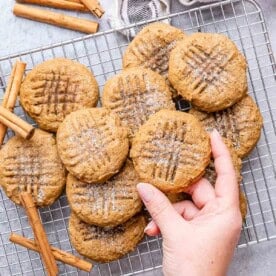cookies on a cooling rack with one hand reaching for a cookie.
