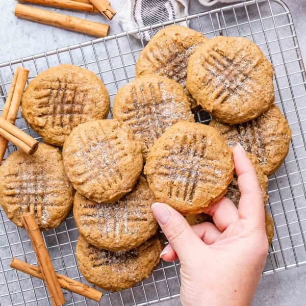 cookies on a cooling rack with one hand reaching for a cookie.