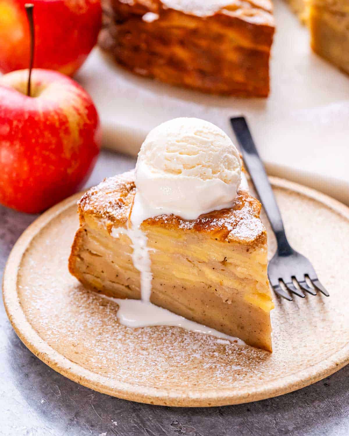 A slice of Invisible Apple Cake on a beige plate with a scoop of vanilla ice cream.