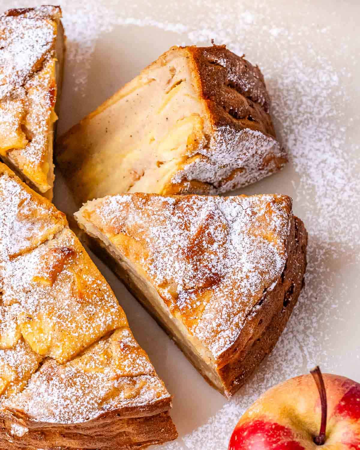 A sliced invisible apple cake, dusted with powdered sugar, on a marble board.