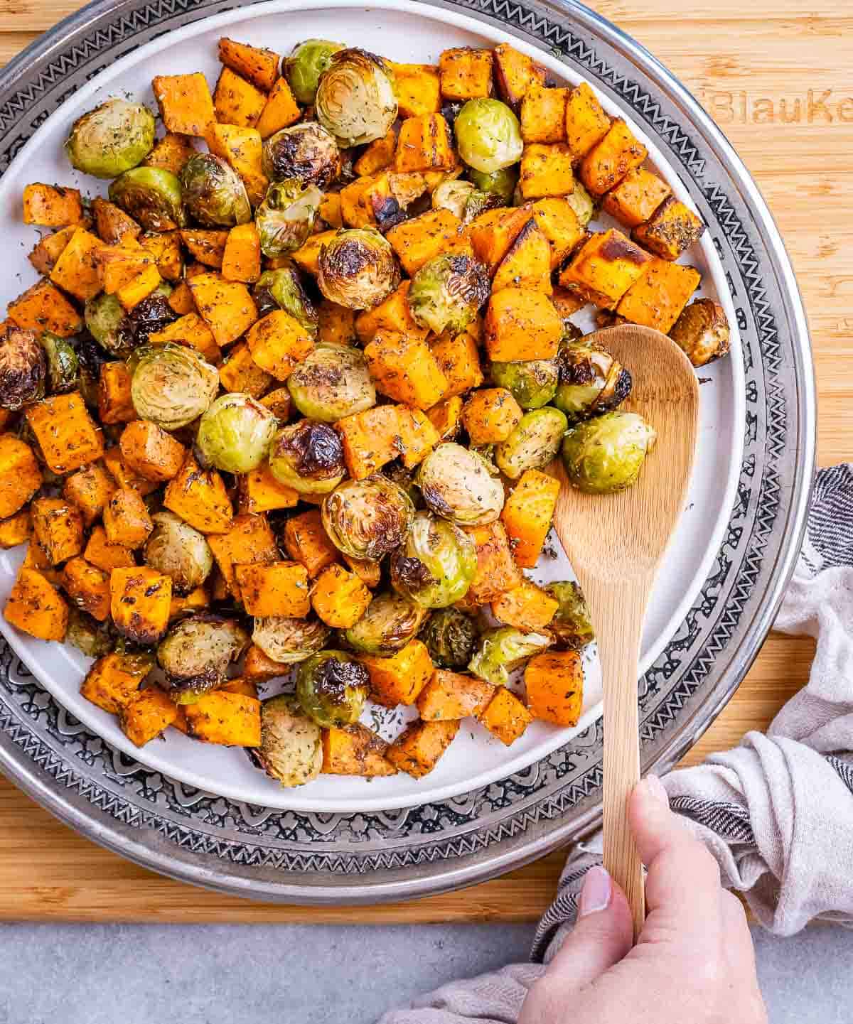 Roasted sweet potatoes and Brussels sprouts in a bowl with a wooden spoon.