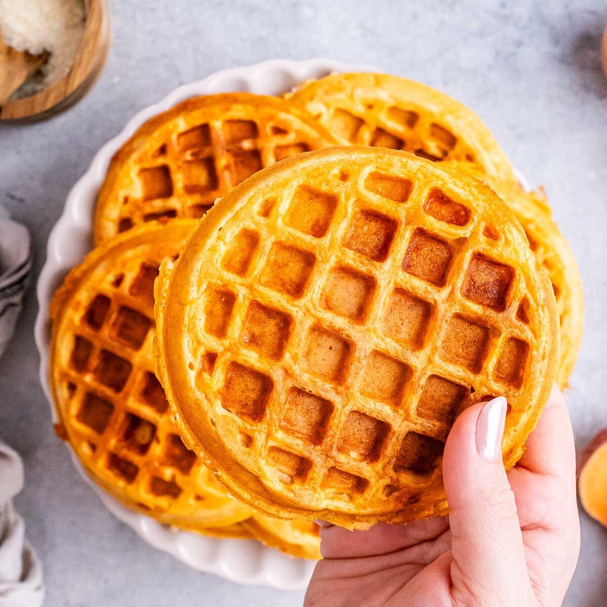 A hand holding a sweet potato waffle over a plate of waffles.