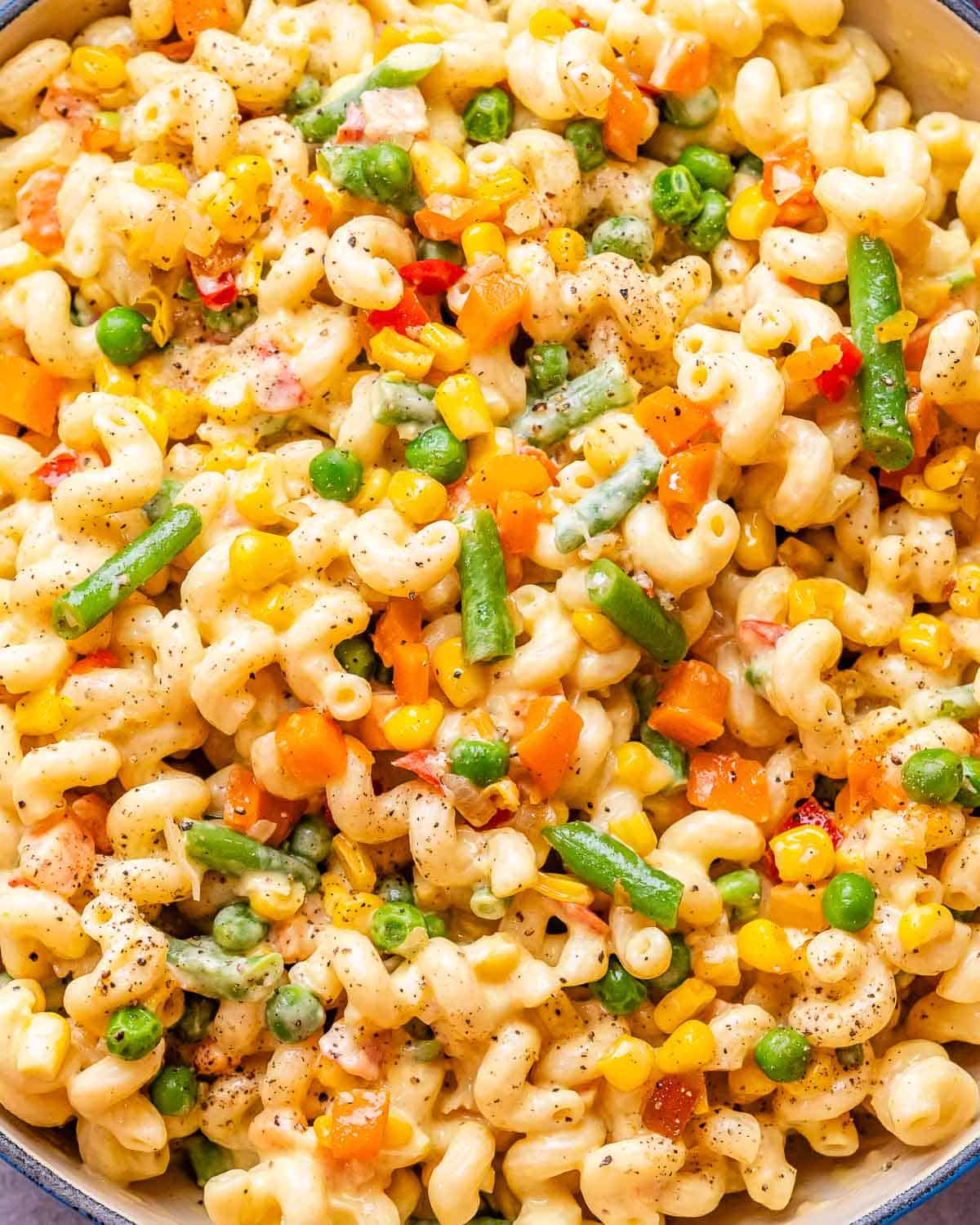 A close up image of veggie mac and cheese with carrots, peas and green beans.