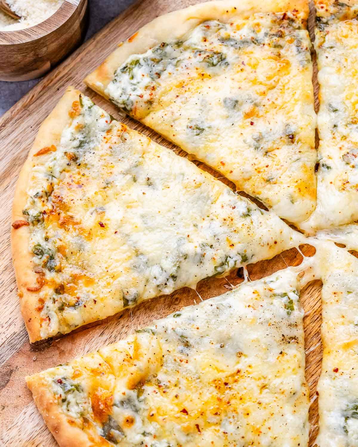 A close up of white pizza sliced into wedges on a wooden board.