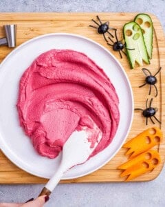 spreading beet hummus over a plate with a spatula.