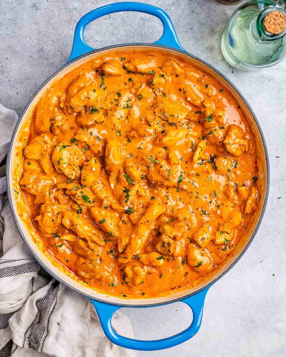 A blue skillet of chicken paprikash with a grey cloth.