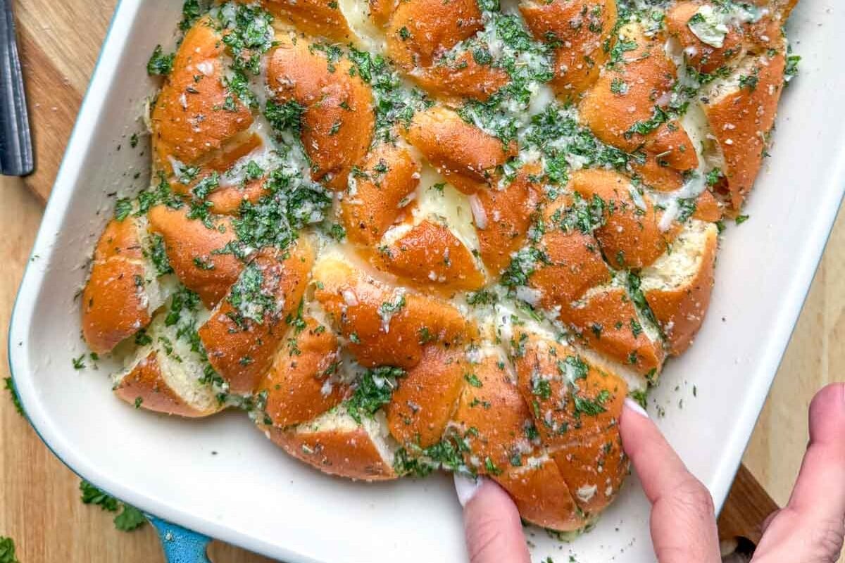 hand grabbing a garlic bread dinner roll from a baking dish.