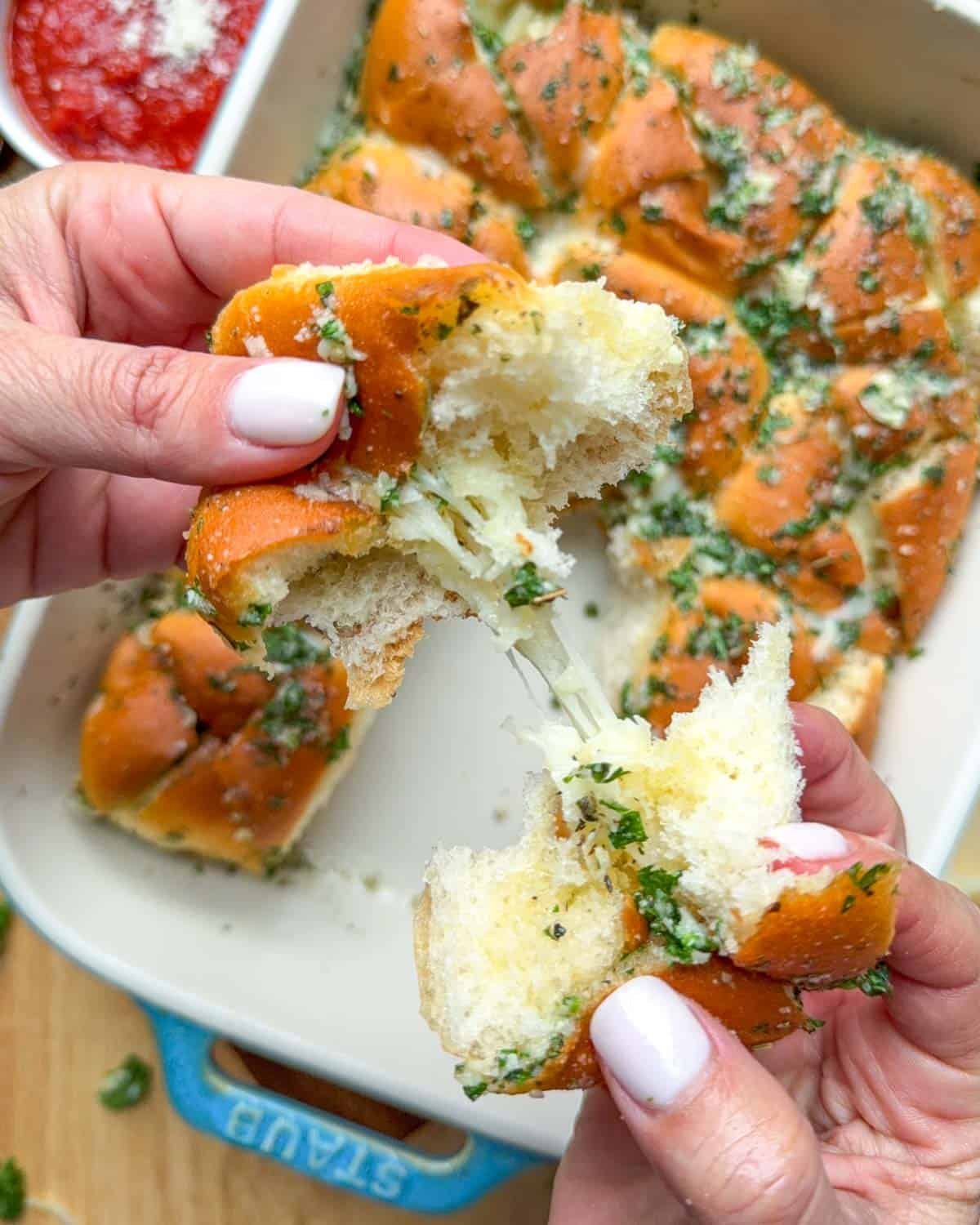 hand pulling apart a dinner roll over a baking dish.