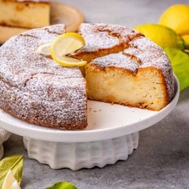 cake on a cake pedestal with a slice taken off it.