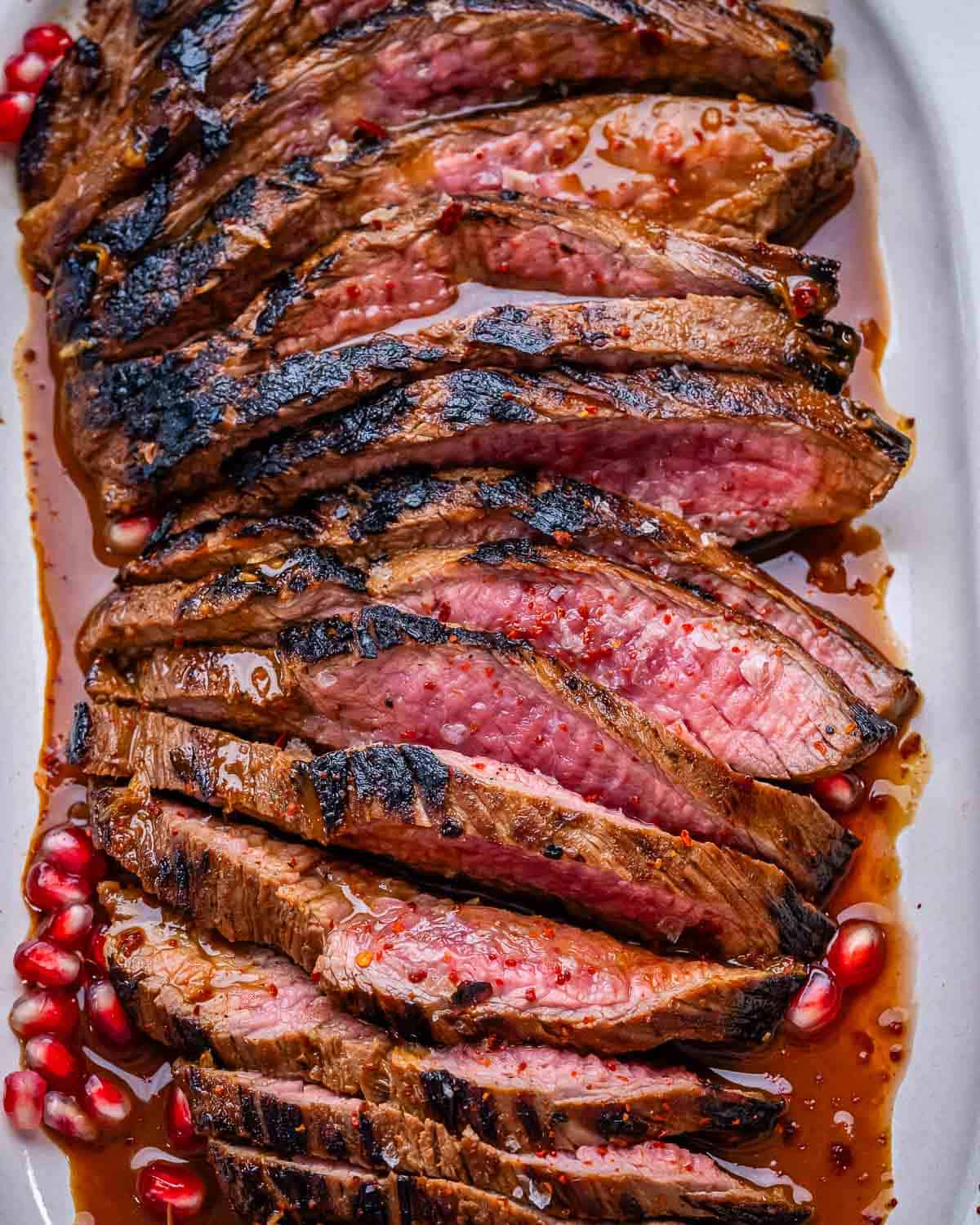 marinated steak on a plate topped with pomegranate arils.