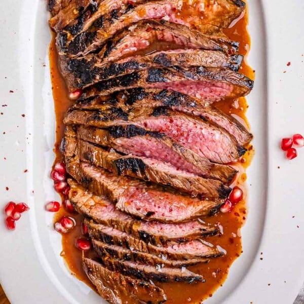 sliced steak on a plate with marinated sauce and pomegranate arils.