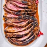 sliced marinated steak on a white plate set in a molasses steak sauce.