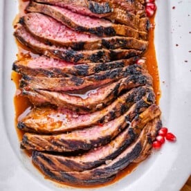 sliced marinated steak on a white plate set in a molasses steak sauce.