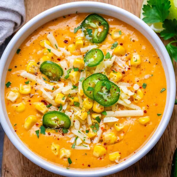 a bowl with mexican street corn soup topped with sliced jalapenos and corn kernels.